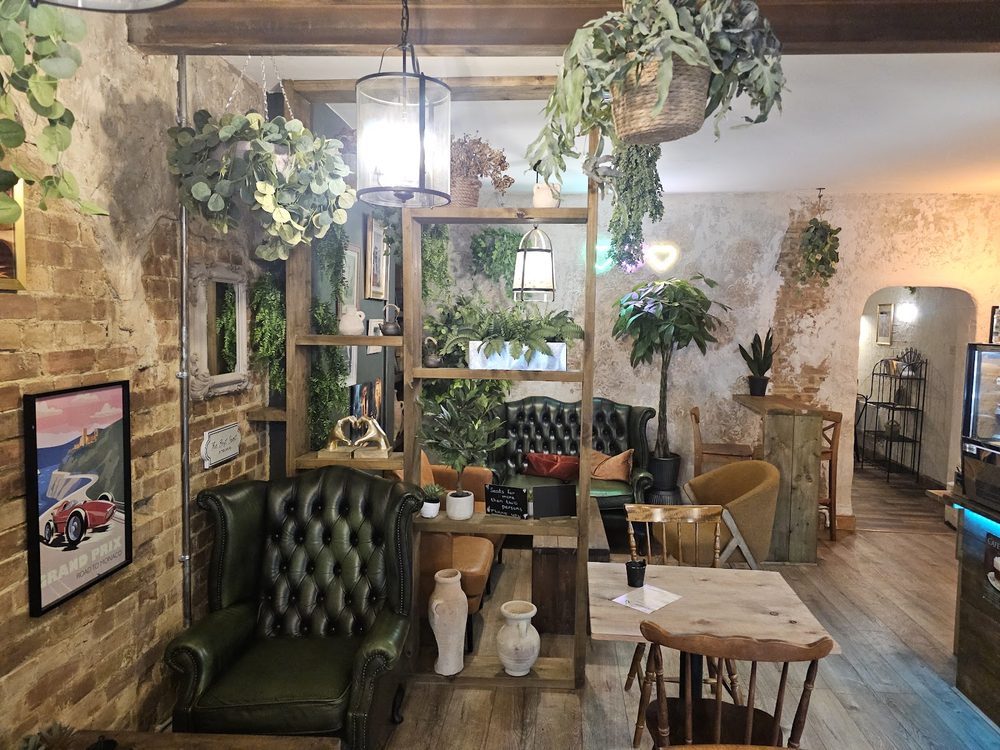 Exposed brick wall, a green leather Chesterfield sofa, plant-filled shelving and framed prints in the seating area
