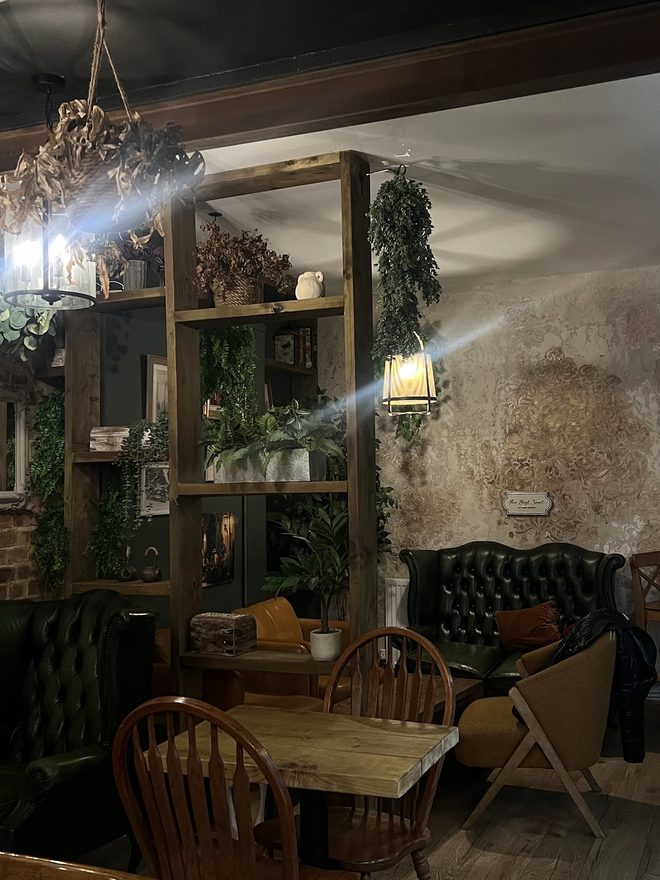 A seating corner with a green Chesterfield sofa, wooden table and chairs, shelving and hanging plants