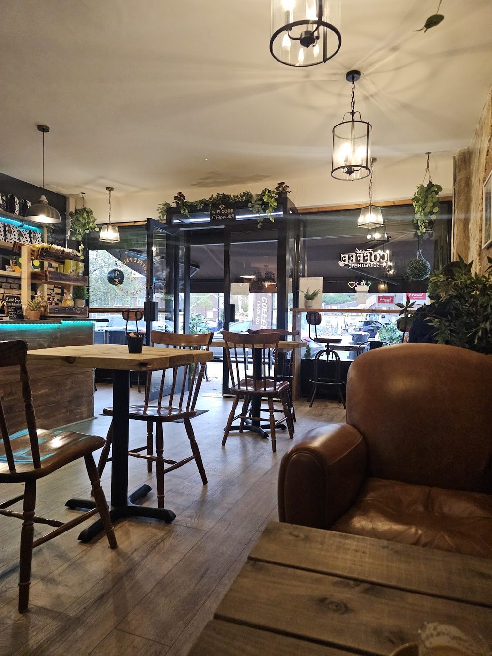 The long cafe floor at Coffee Palette, with pendant lights, wooden tables, a leather armchair and the counter at the far end